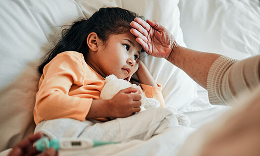 young child laying in bed with guardian feeling forehead and holding a thermometer to check temperature
