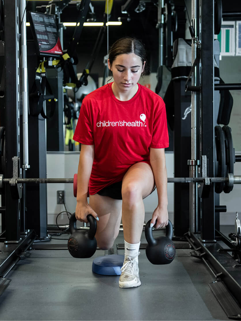 Teenage patient lunging with two kettlebell weights
