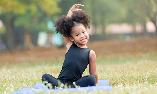 young girl sitting on a yoga mat outside stretching