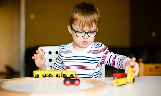 Young boy sitting at a table playing with wooden train toy
