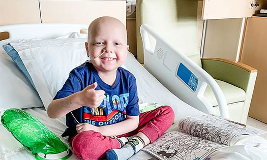 Henry sitting on hospital bed giving a thumbs up with a big smile